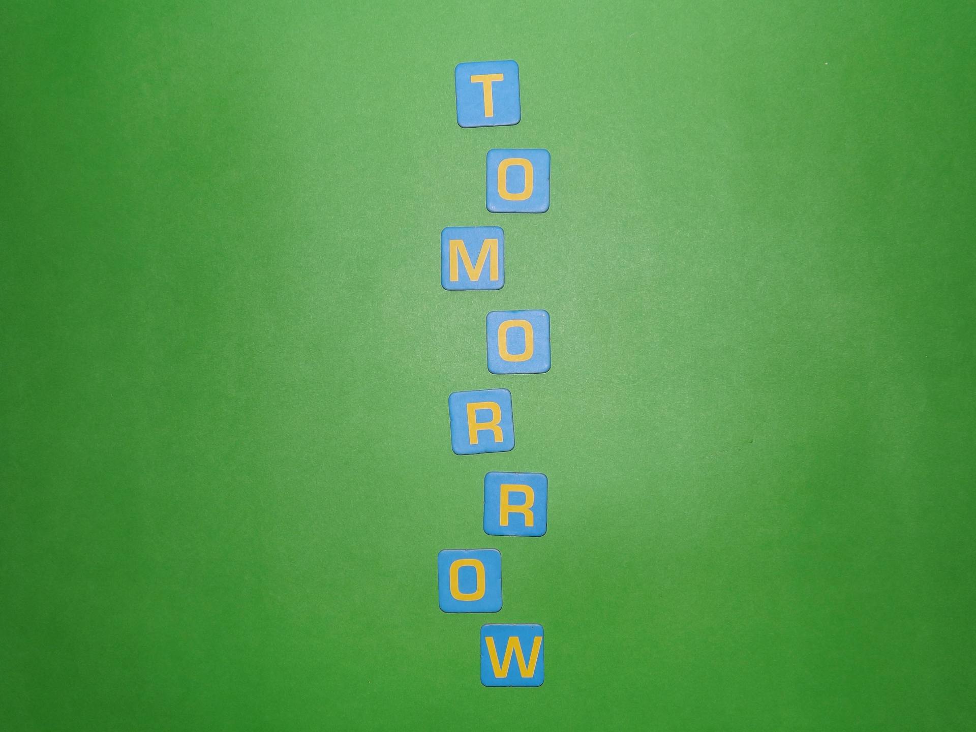 Vertical arrangement of blue letter tiles spelling 'TOMORROW' on a green background.