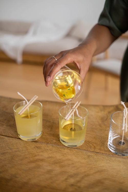 Free A woman carefully pours melted yellow wax into glass containers with wicks. Stock Photo