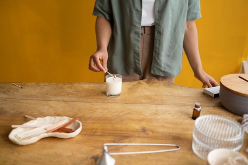 Free A person lights a candle on a wooden table, setting a cozy and calming atmosphere. Stock Photo
