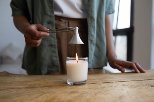 Free A person snuffs a white candle with a metal tool on a rustic wooden table indoors. Stock Photo