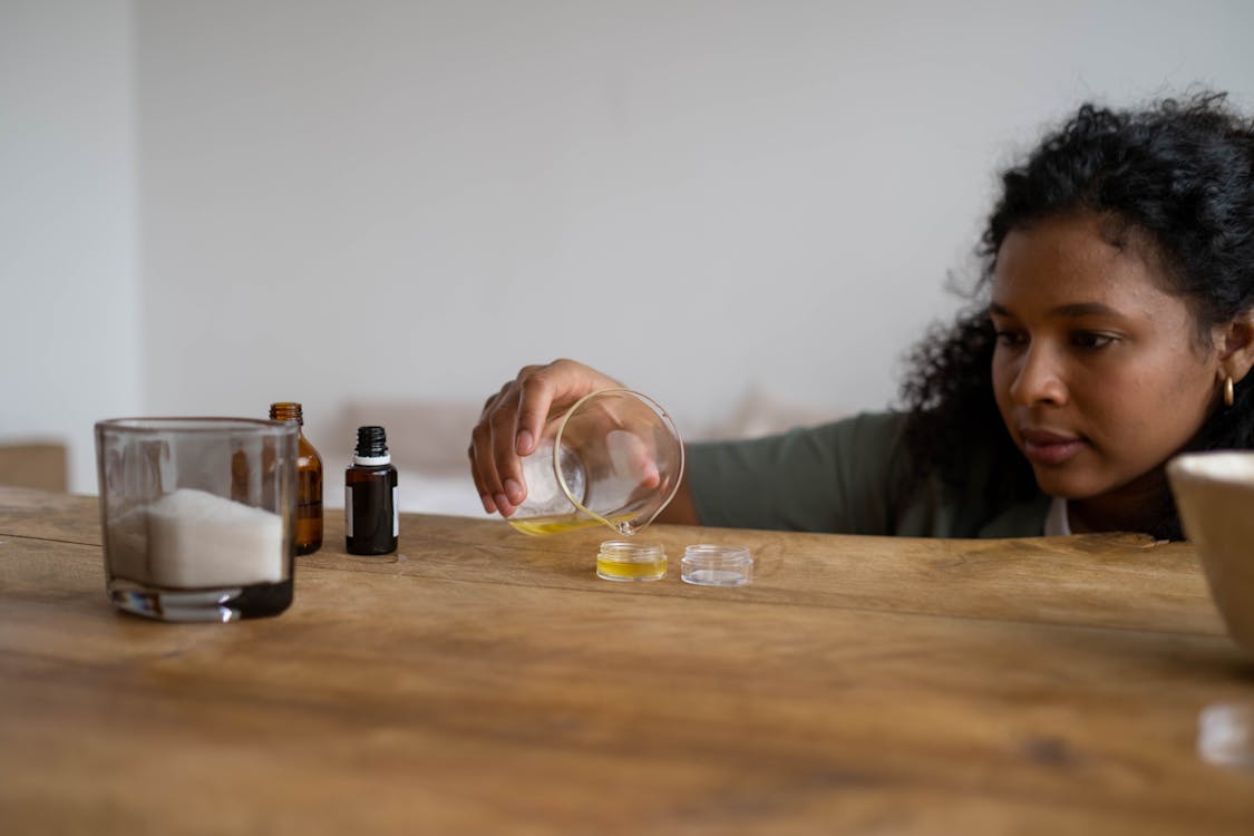 Free A woman mixes ingredients to create natural lip balm indoors, using a wooden table as a workspace. Stock Photo