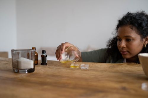 Free A woman mixes ingredients to create natural lip balm indoors, using a wooden table as a workspace. Stock Photo