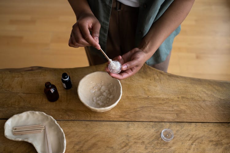 A Person Transferring The Ointment On A Small Container From The Bowl