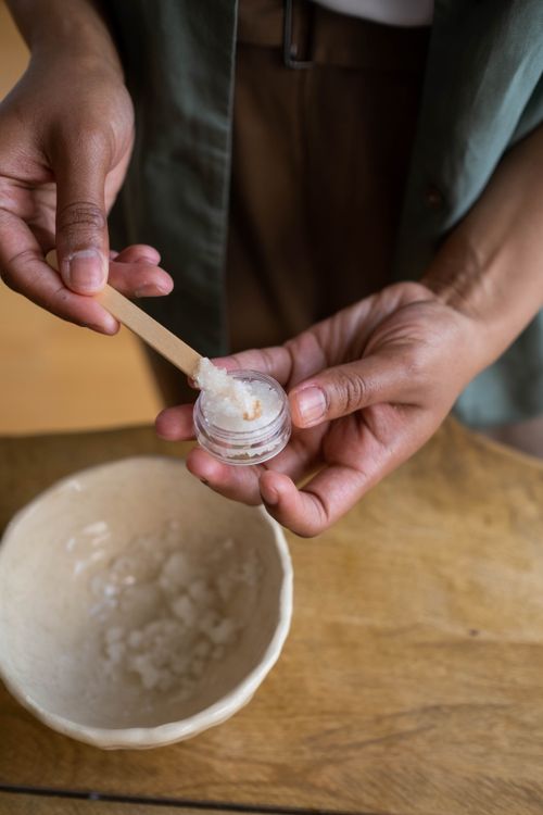 Free A person using a wooden stick to carefully transfer ointment from a bowl into a small container. Stock Photo