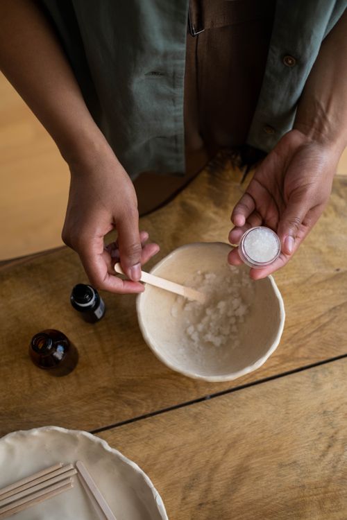 Free Hands preparing a natural body scrub in a rustic setting, featuring jars and mixing tools. Stock Photo