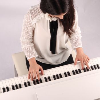 Overhead view of a woman playing piano indoors, focusing on her hands and instrument.（イメージ）