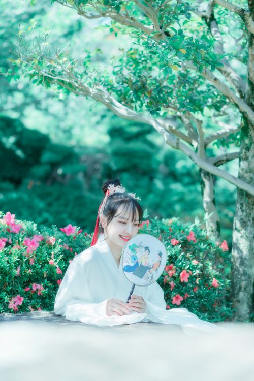 Free A young woman in traditional attire smiles while sitting outdoors in a vibrant garden. Stock Photo