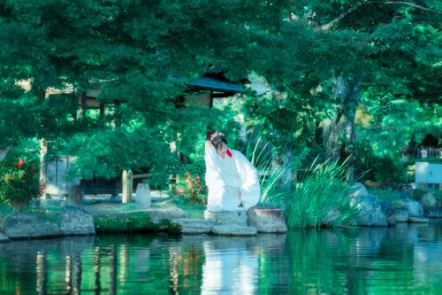 Free Woman in traditional kimono sitting by a peaceful lake in a lush Japanese garden. Stock Photo