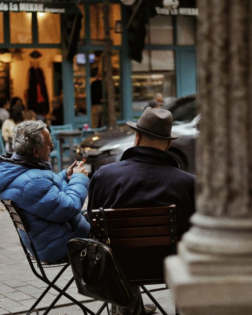Free Two senior men sit on wooden chairs at a cafe in bustling İstanbul street. Stock Photo