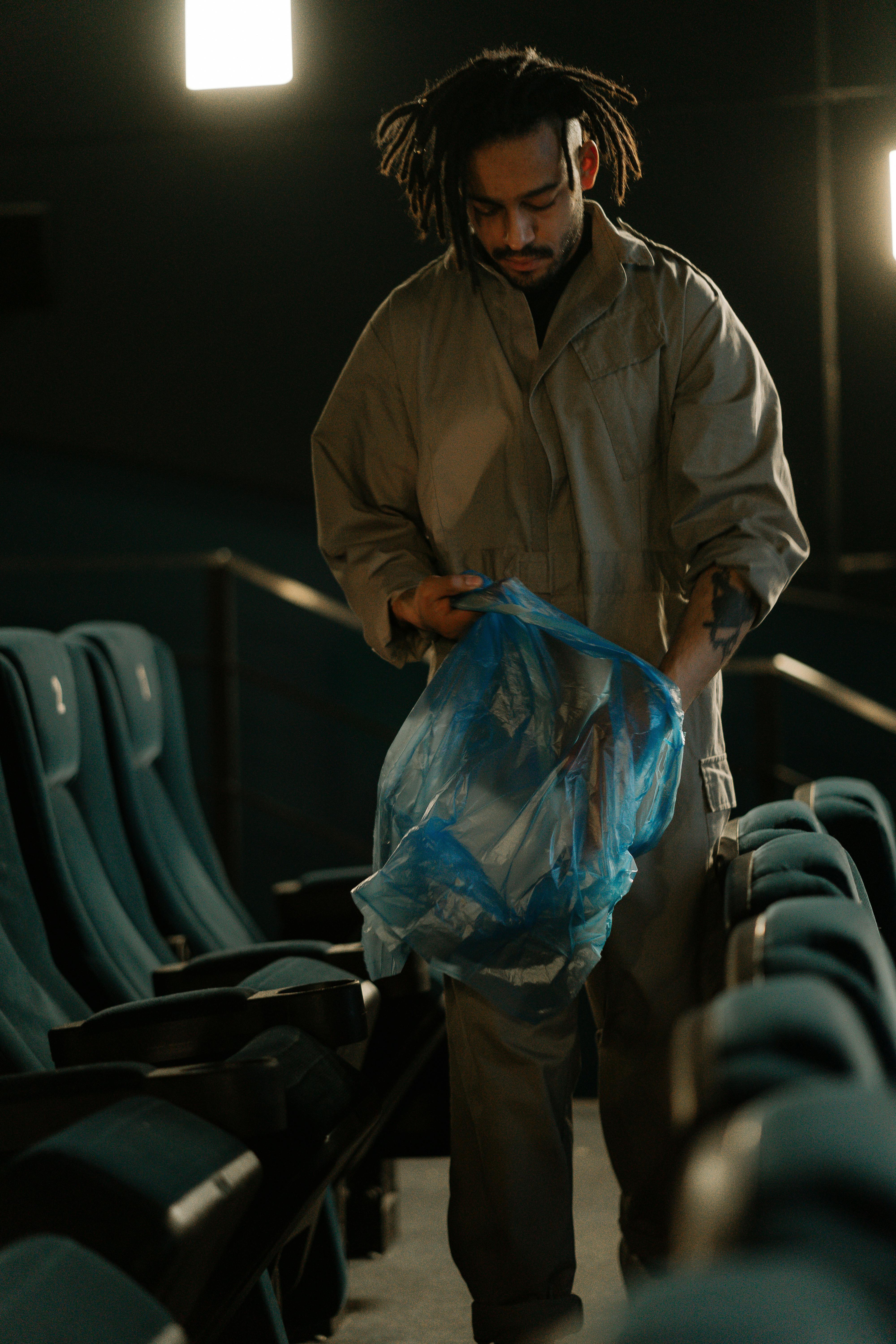 Free A janitor holding a plastic bag cleaning between rows in a dimly lit cinema. Stock Photo