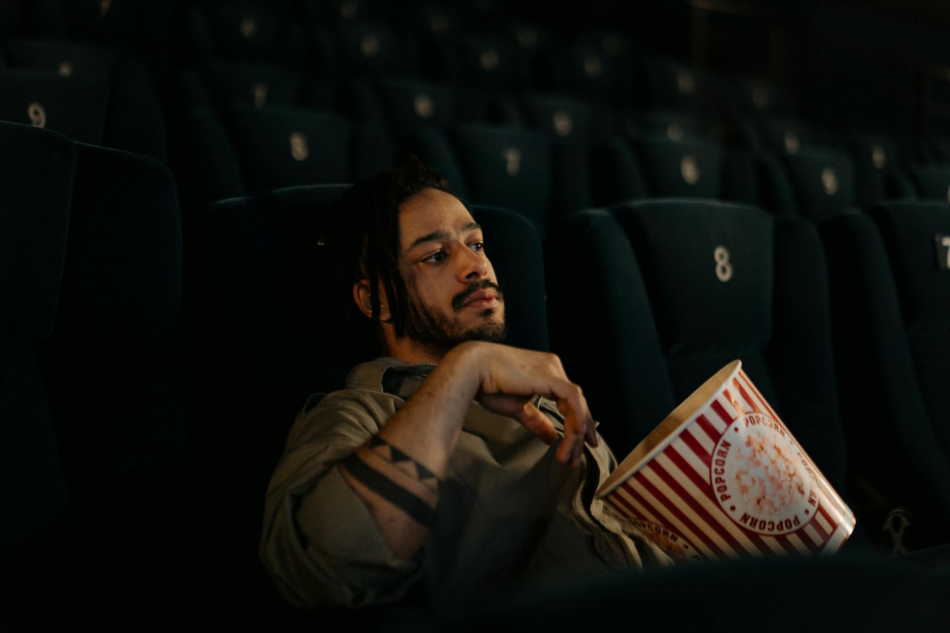 Man sitting alone in a movie theater, holding a large bucket of popcorn.