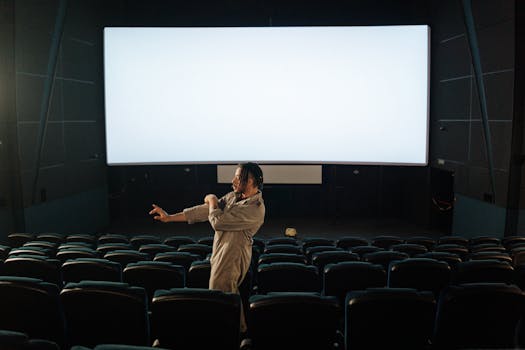 Man standing in an empty movie theater with a blank screen, indoors setting.