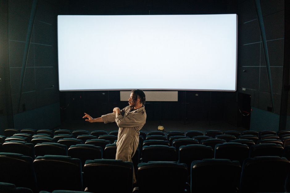 Man standing in an empty movie theater with a blank screen, indoors setting. Man standing in an empty movie theater with a blank screen, indoors setting.