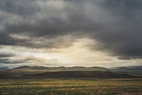 Free Dramatic landscape with rolling hills under a thick overcast sky providing a moody atmosphere. Stock Photo