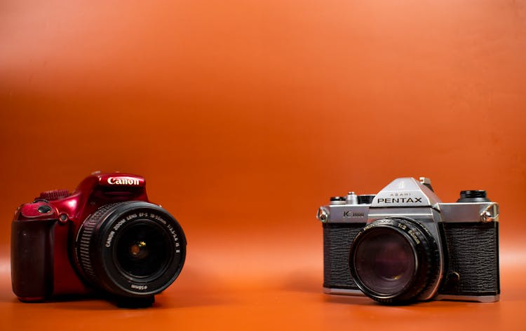 A Red Canon DSLR Camera And A Pentax K1000 SLR Camera