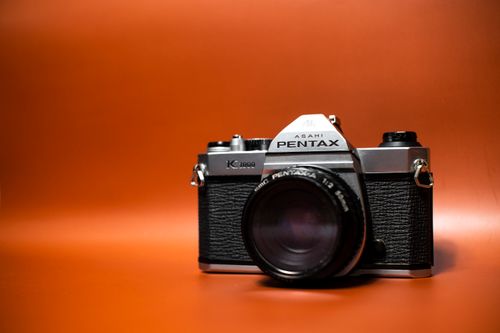 Free Close-up shot of a classic Asahi Pentax camera against an orange backdrop. Stock Photo