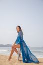 A Woman in a Blue Dress Sitting on a Wooden Stool at the Seashore