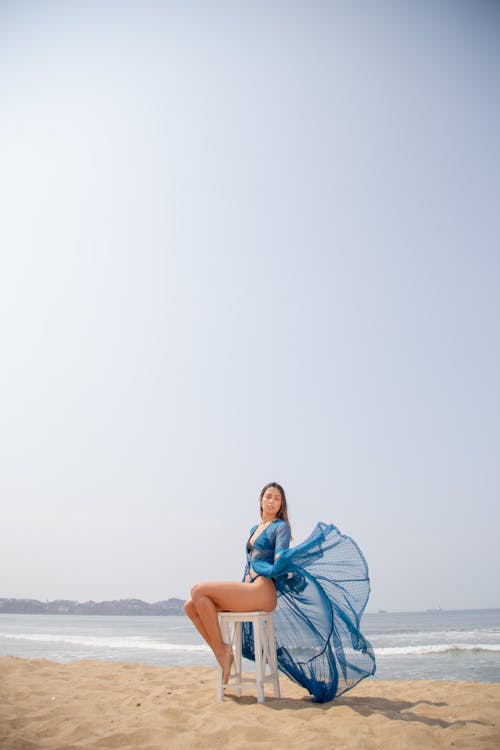 Woman in Blue Sheer Fabric Posing Near the Sea