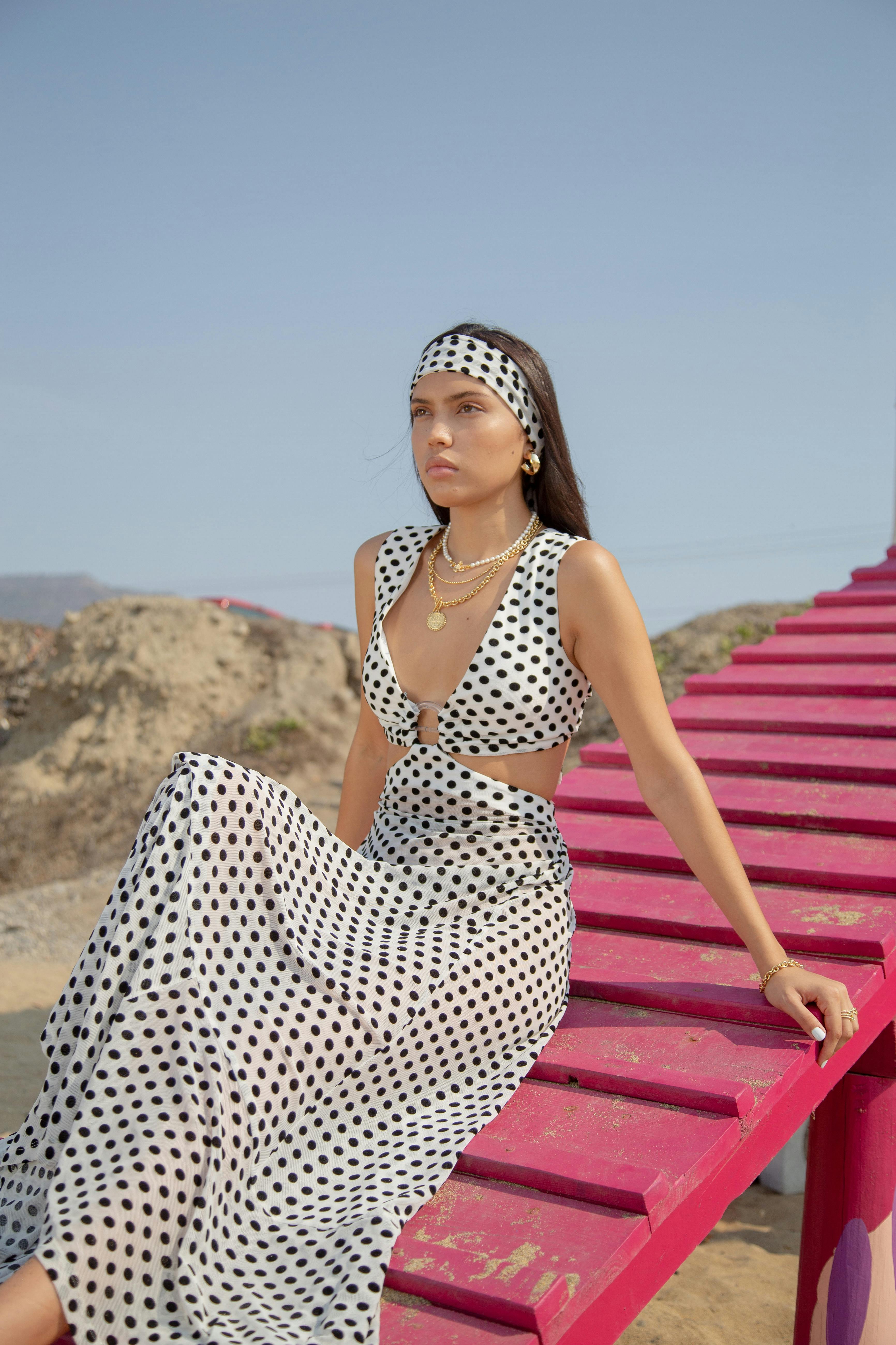 Hispanic woman in polka dot dress sitting on pink structure in sunny outdoor setting.