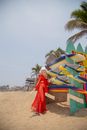 A Woman in Red Dress Standing Beside a Rack of Surfboards on the Beach