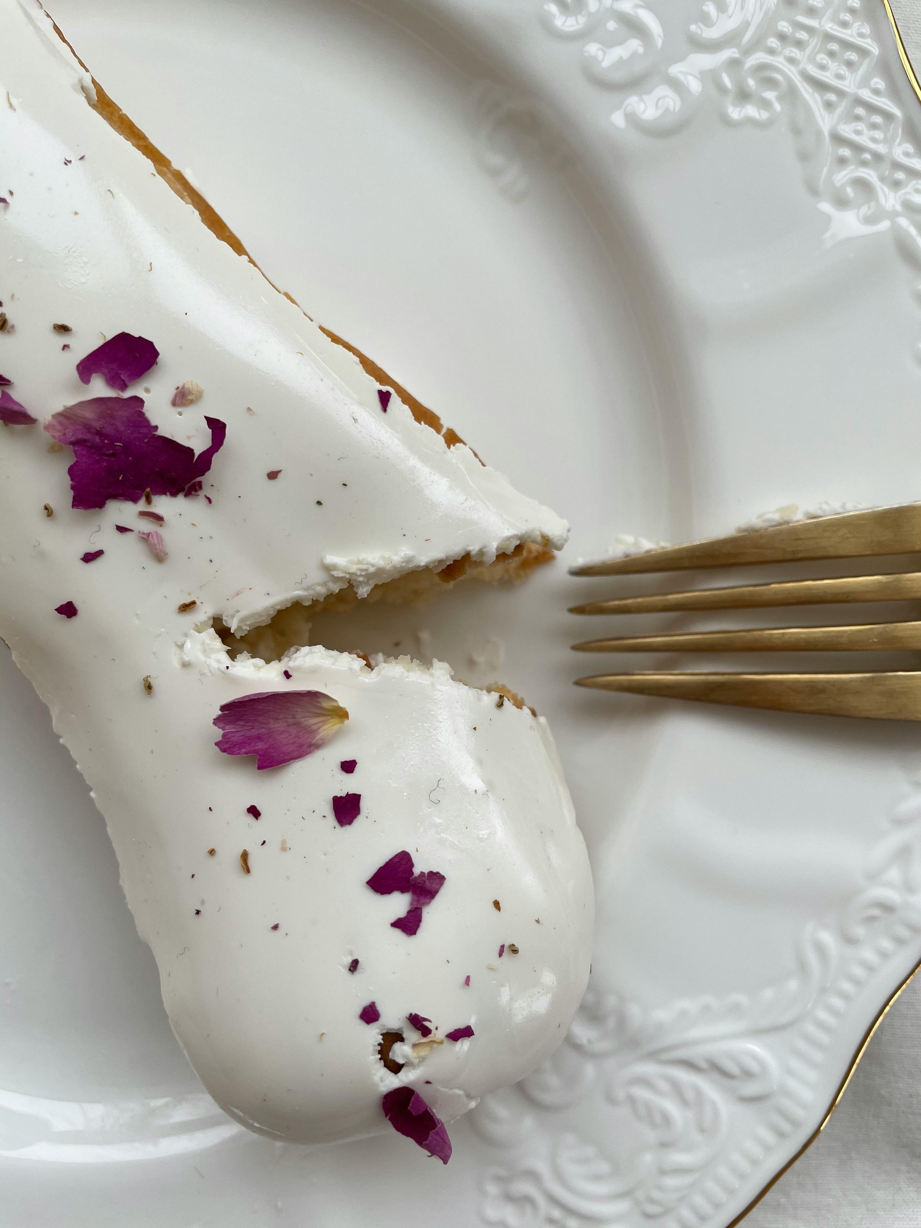 Delicious white dessert with rose petals served elegantly on a white plate, with a golden fork beside.