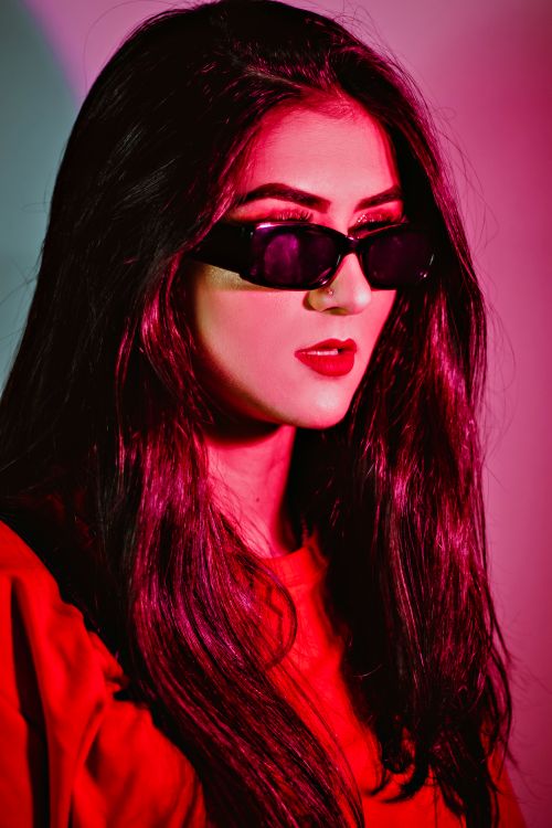 Free Chic and colorful portrait of a woman wearing sunglasses, featuring a vibrant red and pink lighting. Stock Photo