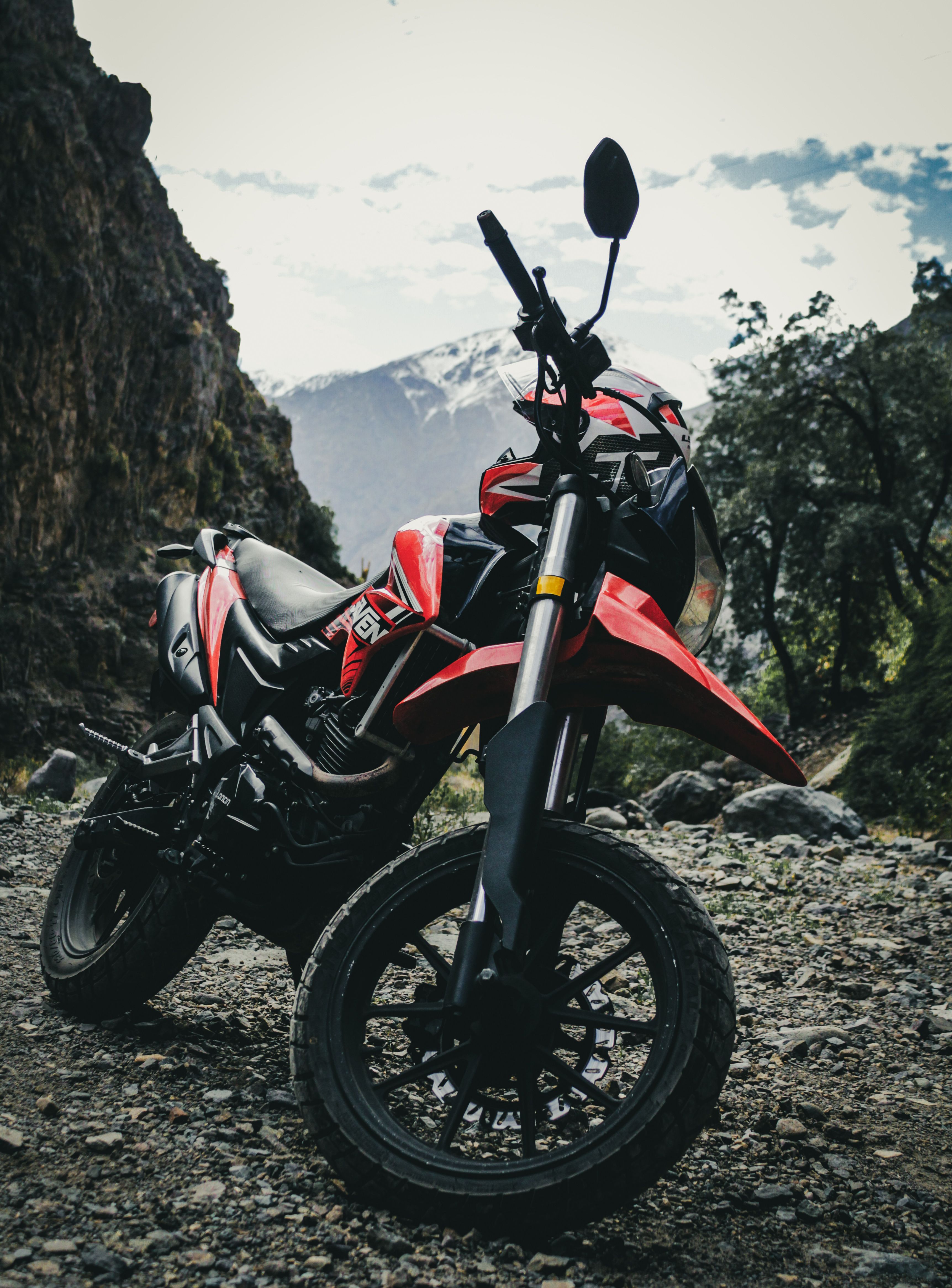 A parked dirt bike on rocky ground with a scenic mountain backdrop.