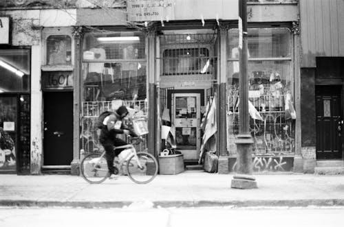 Grayscale Photo of Man Riding a Bicycle on the Sidewalk