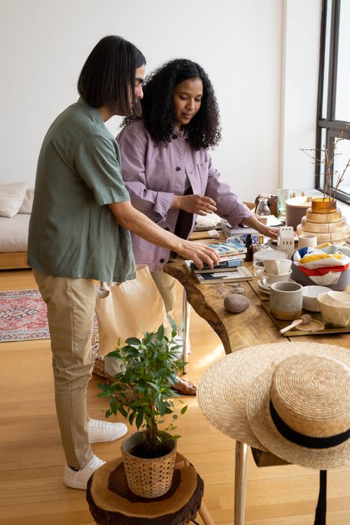 Free Two people working creatively in a cozy studio environment with a variety of objects on the table. Stock Photo