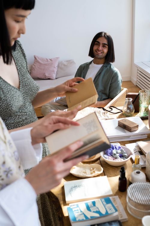 Free Friends enjoying a relaxed afternoon with books in a bright, cozy living room setting. Stock Photo