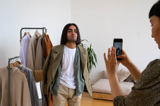 A casual fashion photoshoot indoors featuring friends capturing moments with a smartphone.