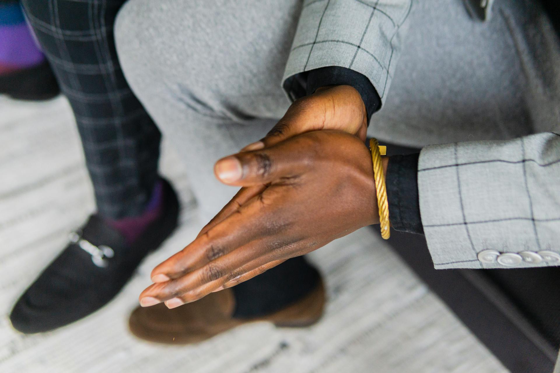 Close-up of a businessman with gold bracelet rubbing hands in a tailored suit.