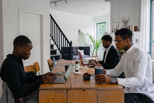 Three young professionals working in a contemporary office setting with laptops and devices.