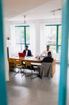 Three men engaged in a professional meeting around a table in a modern office space.
