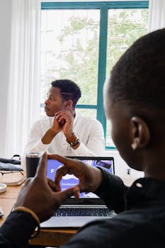 Two black men engaged in a thoughtful discussion during a business meeting in an office setting.