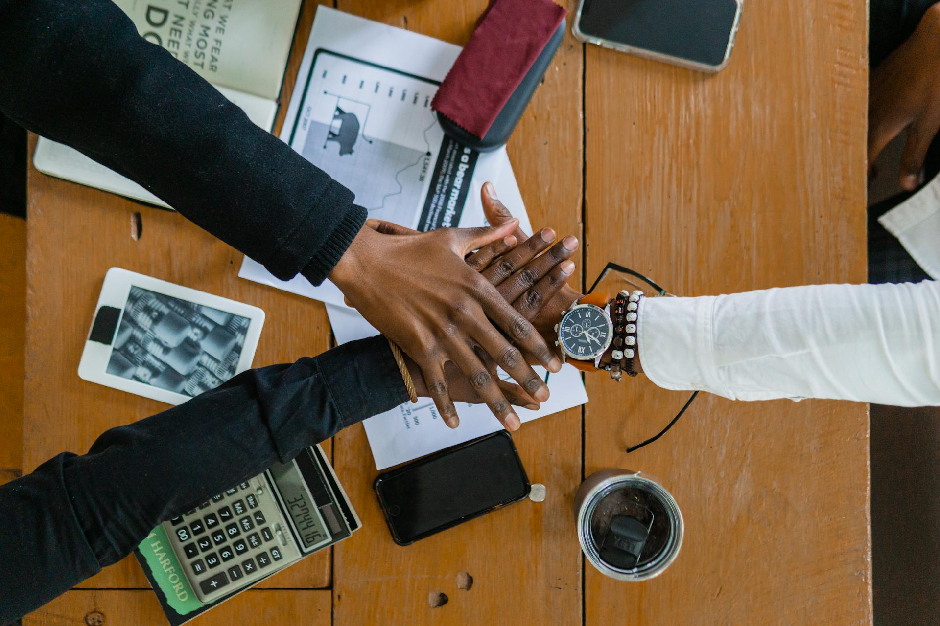 Overhead view of diverse hands stacked in teamwork over a desk with documents and gadgets.