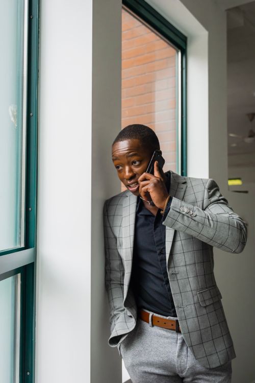Free Stylish man in gray suit making a phone call by a window indoors. Stock Photo