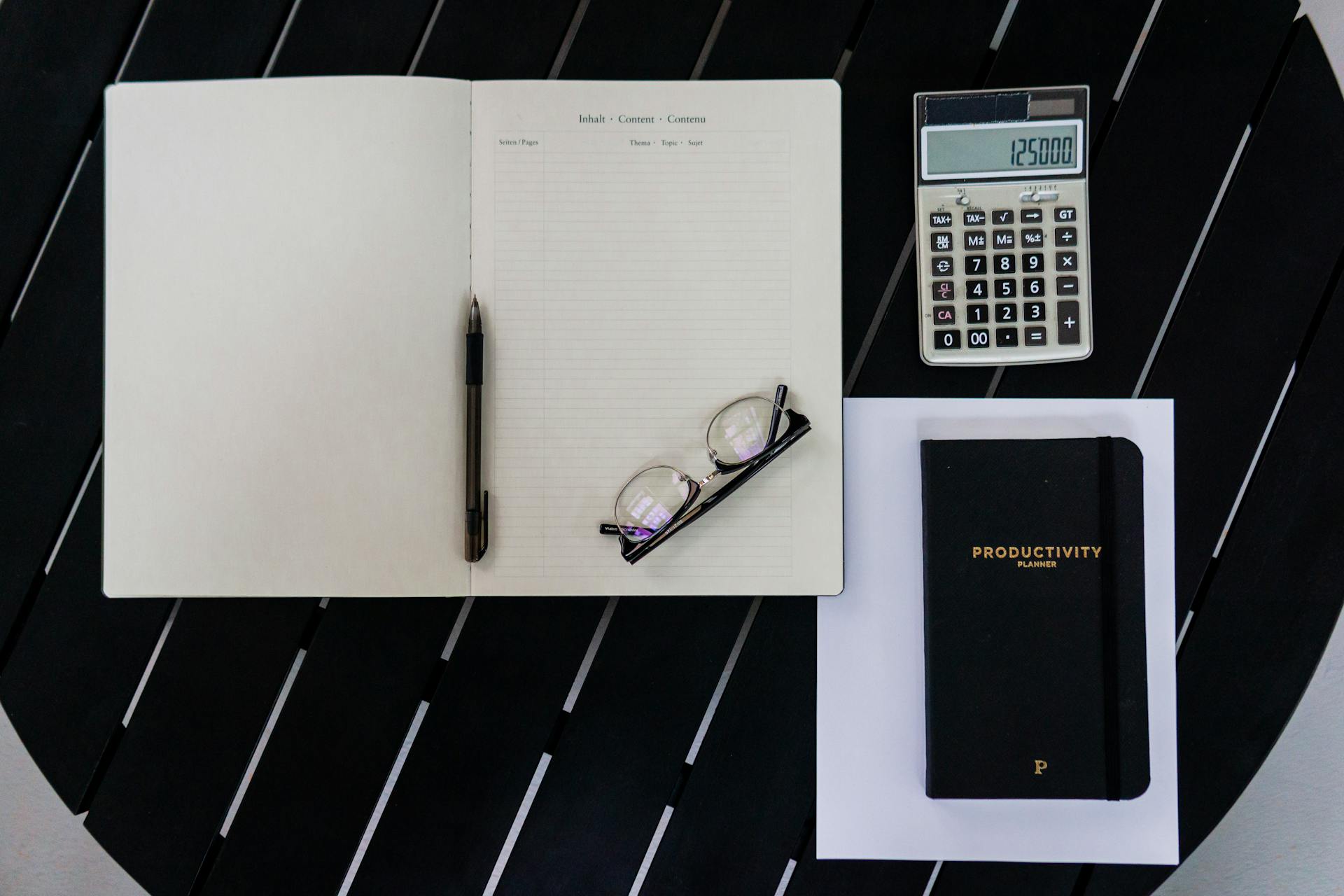 Flat lay of a productivity planner with calculator, pen, and eyeglasses for efficient office work.