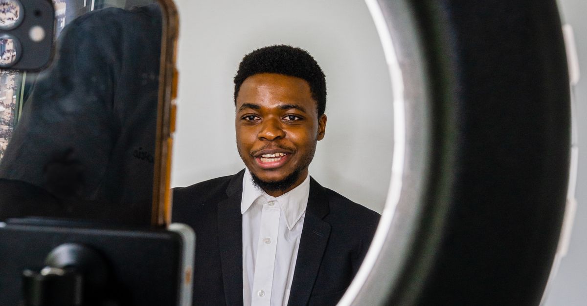 A young man in a blazer recording himself on a smartphone with a ring light