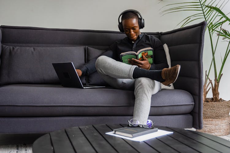 Man Sitting On Couch Wearing Headphones While Reading Book