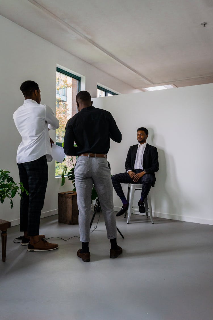 A Man In A Suit Sitting Near Other Men