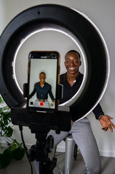 Smiling African American man recording video indoors using a smartphone and ring light setup.