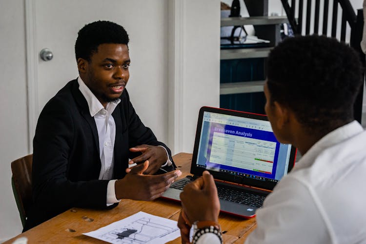 Man In A Black Suit Talking Near A Laptop