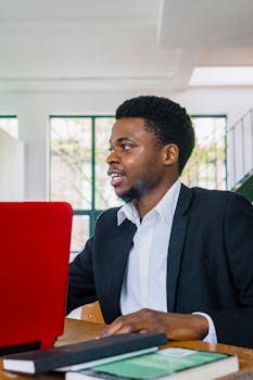 Portrait of a black businessman in a suit working on a red laptop indoors.