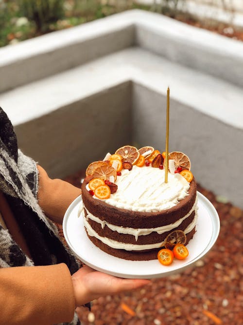 Free Close-up of a Person Holding a Layer Cake with Oranges on Top  Stock Photo