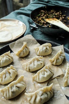 Close-up of handmade uncooked dumplings on parchment paper with filling in background.