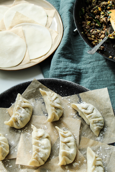 Close-up of raw dumplings on a tray with ingredients and dough wrappers nearby.