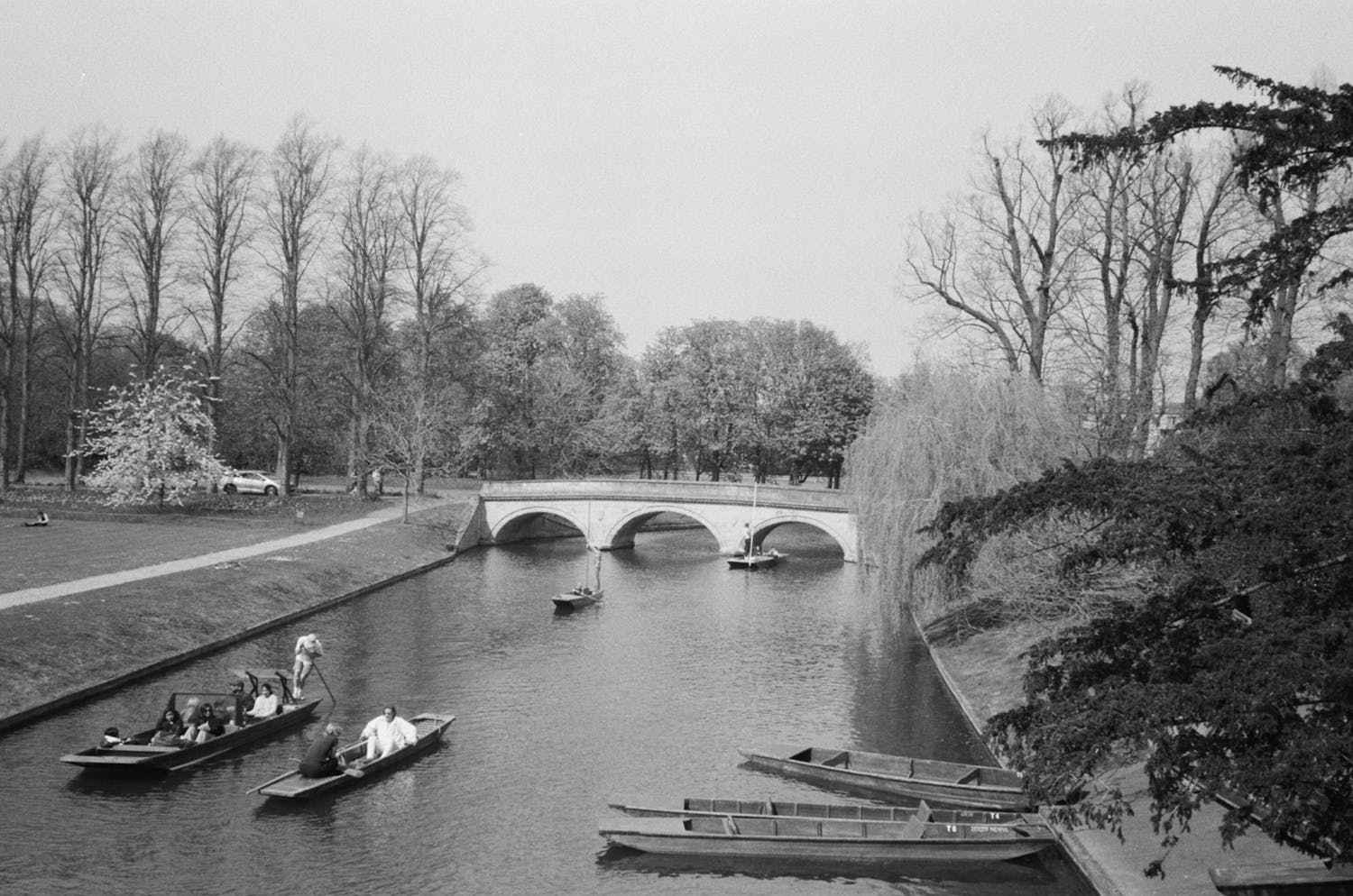 Black and white photo of punts on River Cam with scenic bridge view