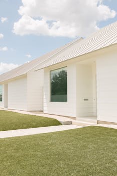 A modern white house in Houston with large glass windows and a sleek design, under a clear blue sky.