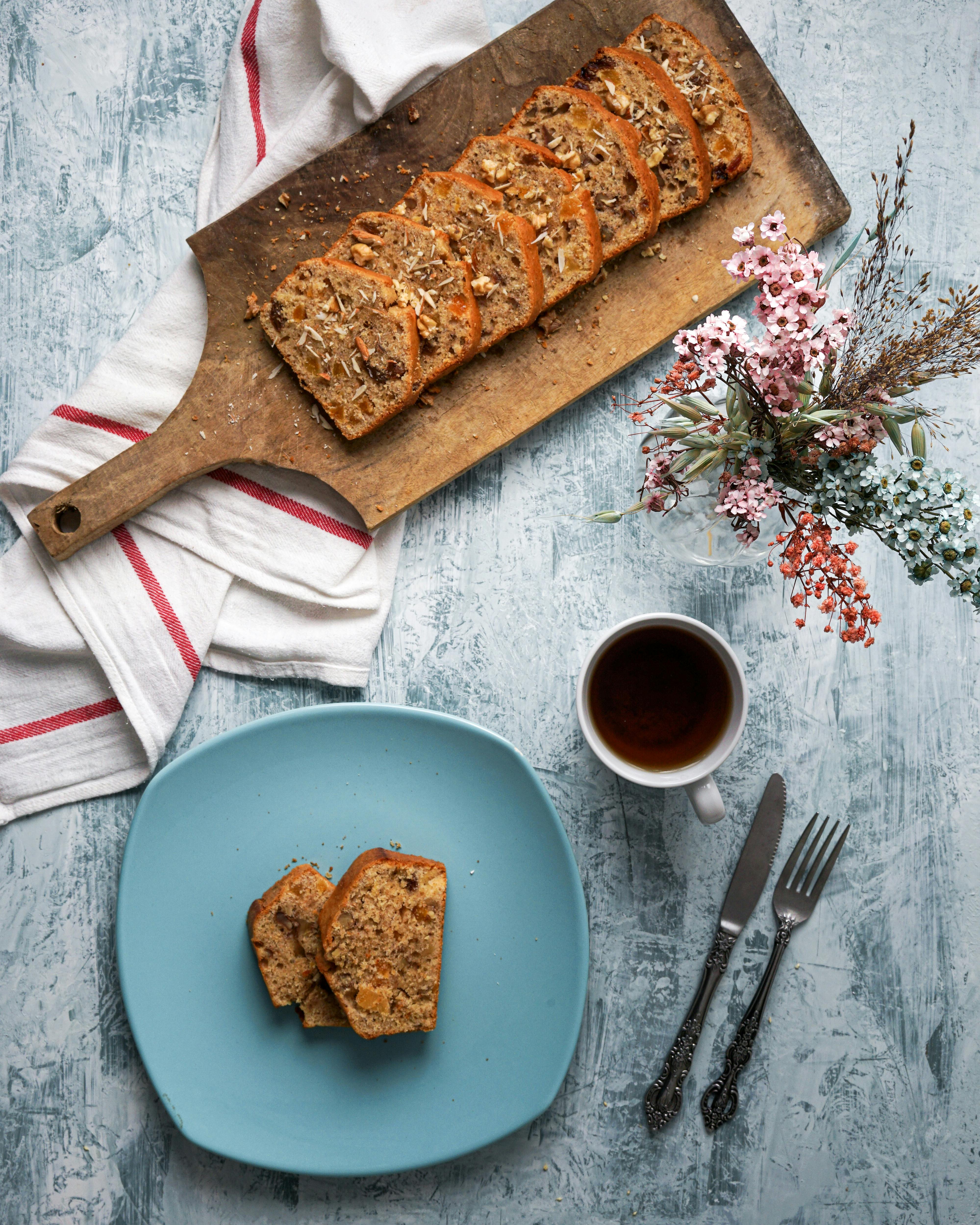 A rustic flat lay of sliced bread, tea, and flowers on a textured surface.